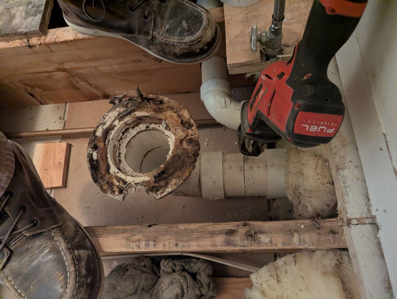 Broken toilet flange found under the bathroom floor above a stained kitchen ceiling.