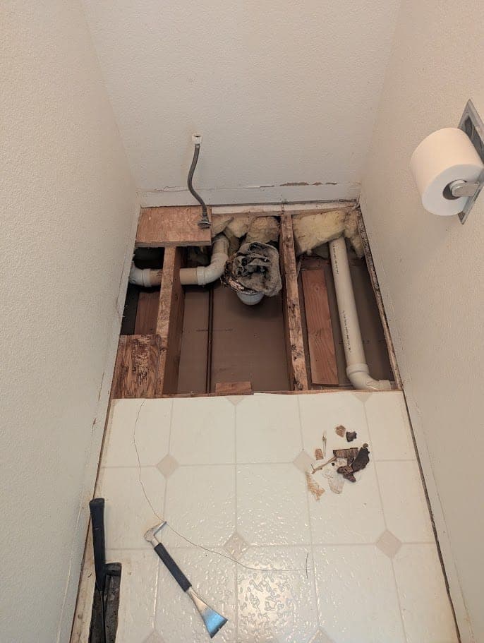 Bathroom floor opened around the toilet drain, with linoleum pulled back and the damaged subfloor cut out, during a Fort Collins repair