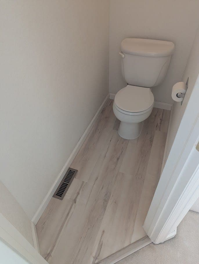 Reinstalled toilet on new flooring, with baseboards and a transition strip to the carpet, after the Fort Collins repair